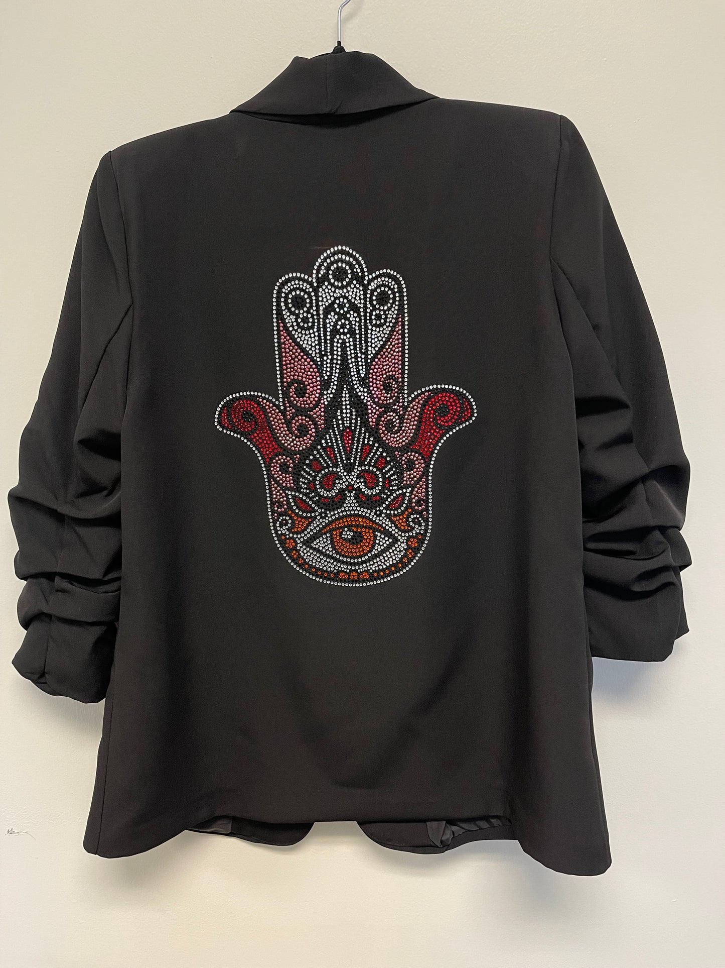 A black blazer with ruched sleeves and a crystal pink hamsa design on the back, featuring a shawl lapel and open front.
