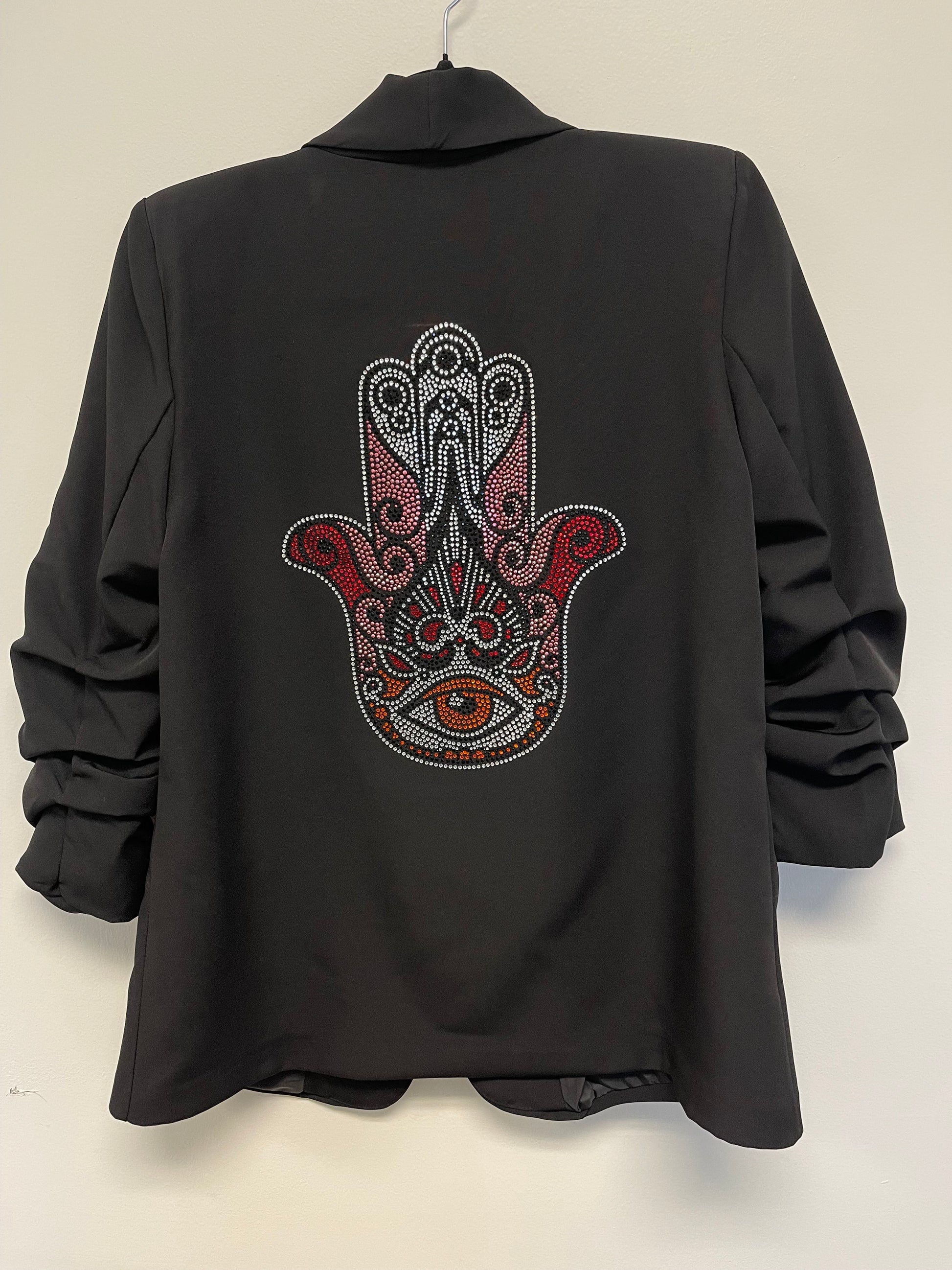 A black blazer with ruched sleeves and a crystal pink hamsa design on the back, featuring a shawl lapel and open front.